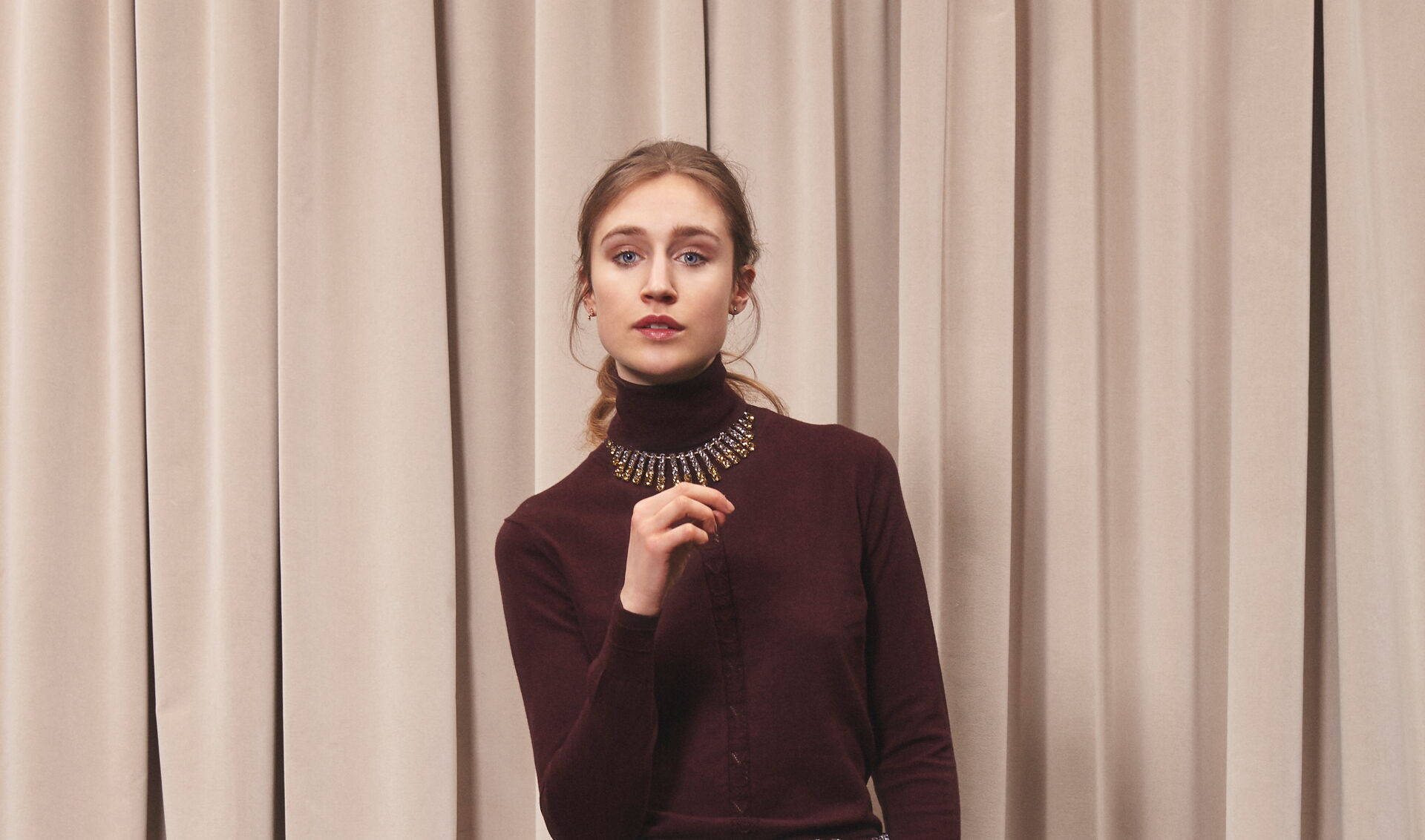 Junge Frau in dunklem bordeauxroten Rollkragen-Pullover mit breitem glitzernden Halsschmuck