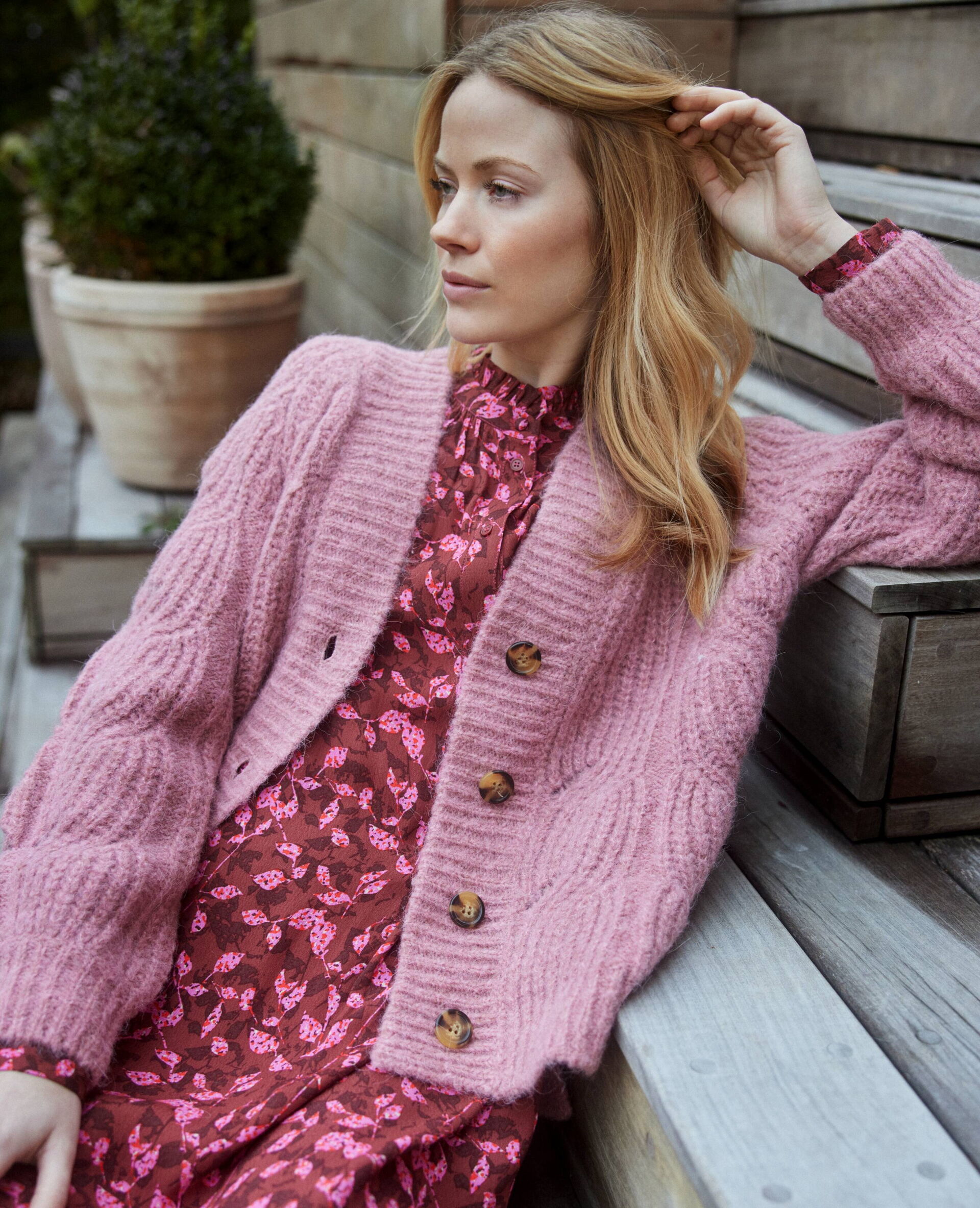 Junge Frau in einem pinken Kleid mit floralem Muster und Strickjacke in der Farbe rosa