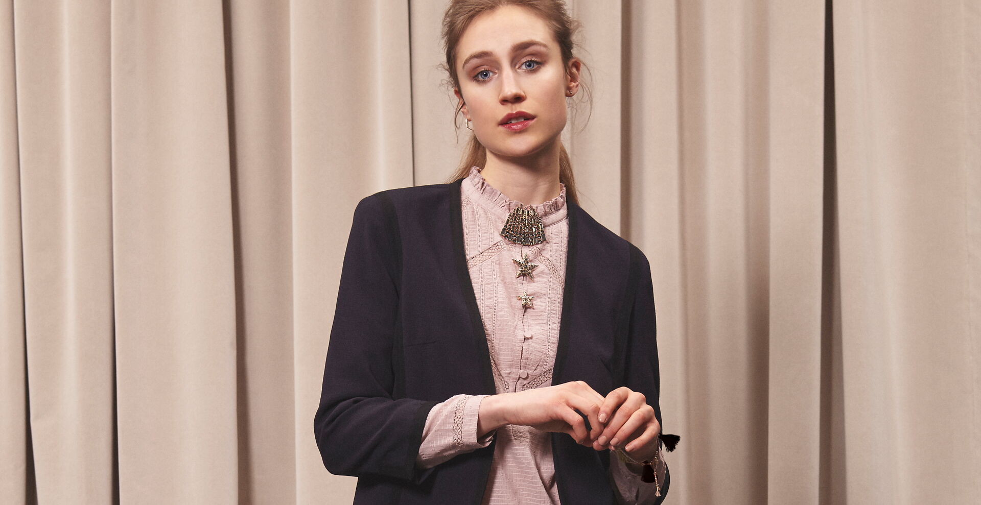 Junge Frau trägt rosefarbene Bluse mit Schmuck-Kragen und dunklen Blazer mit