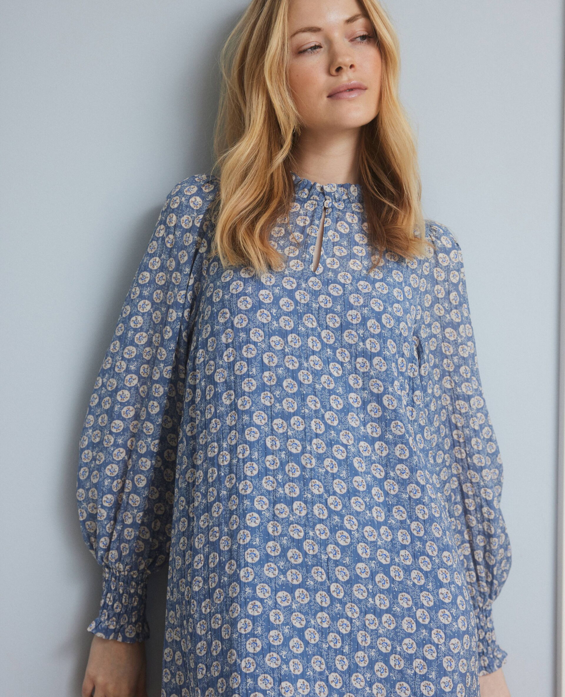 Blonde Frau in einer weiten blauen Bluse mit breit-gerüschtem Saum und weißen gepunktetem floralen Muster